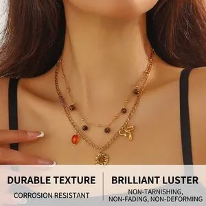 Detail of double-layer gold necklace with tiger eye pendant and bowknot charm on model