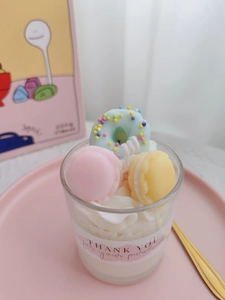 Detail of handmade soy candle with blue donut and macarons in a glass cup dessert design