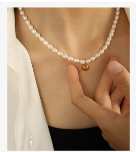 Detailed view of a freshwater rice pearl necklace with a golden ball pendant on a model