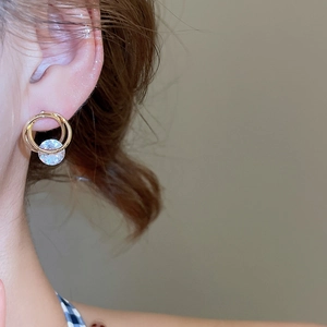 Detailed close-up of a golden double-loop earring with a sparkling clear zircon pendant