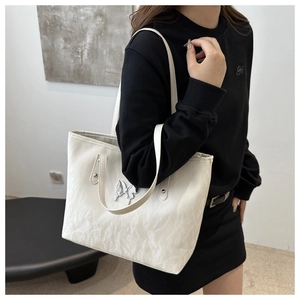 Close-up of beige pleated tote bag featuring a prominent silver butterfly ornament