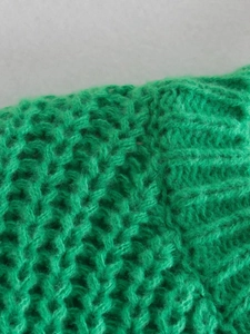 Dettaglio ravvicinato del maglione verde in maglia grossa con trama intrecciata e coste