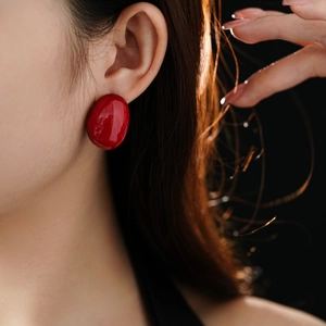 Close-up of a model wearing minimalist bright red enamel oval stud earring on dark background