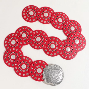Macro detail of red leather round discs with silver floral buckles on a vintage belt