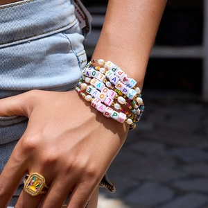 Close-up of stacked colorful beaded bracelets with LOVE and HAPPY letter beads and pearls