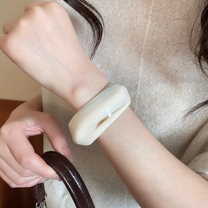 Close-up of an ivory acrylic wide bangle with smooth organic design worn by a model