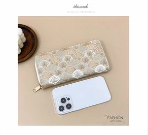 Detailed close-up of beige shell pattern embroidery and gold zipper on long wallet