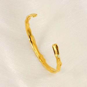 Detail view of gold wave-patterned hammered cuff bracelet on white silk fabric background