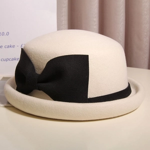 Macro detail of beige wool felt bowler hat featuring a large elegant black bow accent