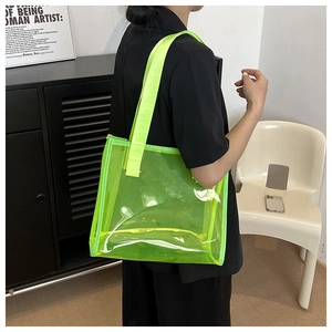 Detailed view of neon green transparent PVC tote bag worn over the shoulder by a model