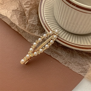 Detailed view of elegant gold-plated hair clip with white pearls and sparkling rhinestones