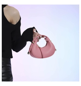Close-up of pink crescent handbag in lychee leather with gold metal hardware and tassel