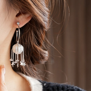 Gros plan de boucles d'oreilles en argent avec pampilles d'étoiles et perle en cage
