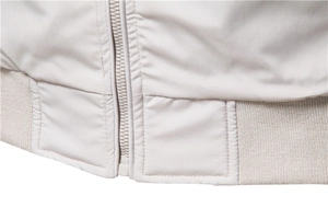 Detail view of smooth nylon zipper and ribbed knit hem on a beige bomber jacket