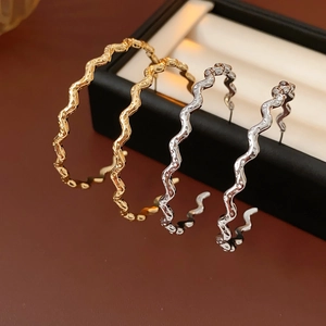 Detail of wavy C-shape gold and silver hoop earrings in a black premium jewelry gift box