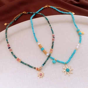 Detail of bohemian beaded necklace with sun pendant and tiny gold lucky charm tag