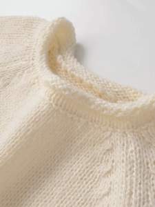 Detailaufnahme des gerippten Rundhalsausschnitts am cremefarbenen Grobstrickpullover