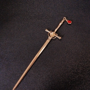 Detailed close-up of a golden sword-shaped hair pin with a red teardrop gemstone charm
