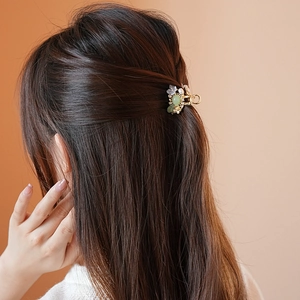 Detail view of flower hair claw with green stones and pearls worn on half-up hair style