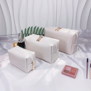 Three-piece white pearl letter makeup bag set with gold zippers on silk background