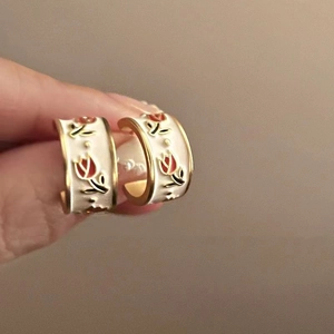 Close-up of gold-plated tulip flower earrings with white enamel and red floral details