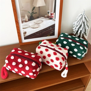 Three plush large capacity cosmetic bags with polka dots and pompom zippers on wood shelf