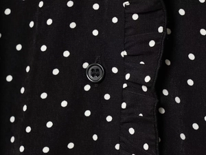 Detail of black polka dot dress featuring a classic button and ruffled edge trim