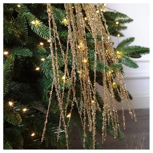 Golden beaded fringe garland draped on a glowing Christmas tree with warm LED lighting