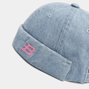 Close-up of pink embroidered letter B on light blue washed denim docker cap texture