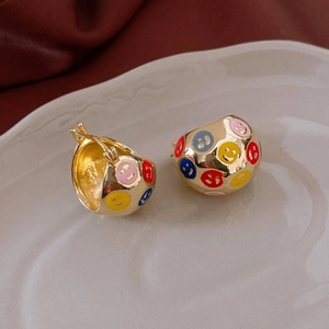 Close-up of golden huggie hoop earrings with colorful smiling faces on a ceramic tray