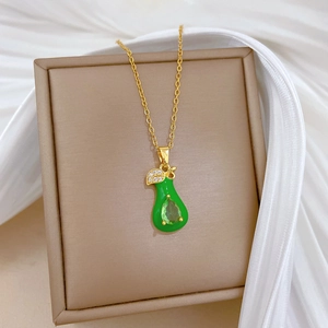 Detail of a gold necklace with green pear pendant and leaf detail on white satin