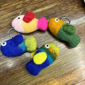 Top view of four colorful handmade wool felt fish keychains on a dark wooden table