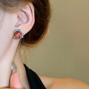 Detail of elegant earrings with red round-cut gemstones and a sparkling diamond halo