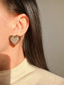 Détail d'une boucle d'oreille cœur dorée avec pavé de zircons brillants portée par un mannequin