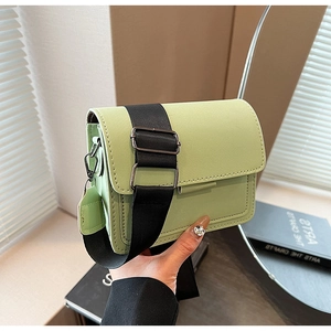 Close-up of a light green small square bag with a wide black adjustable fabric strap
