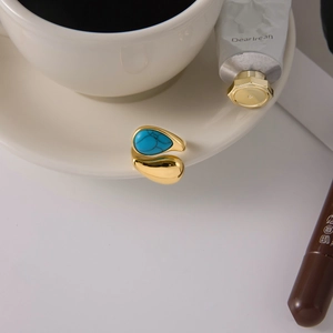 Gold open ring with turquoise teardrop stone on white ceramic coffee cup edge