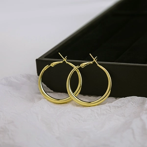 Close-up of classic polished golden hoop earrings on a black jewelry storage box