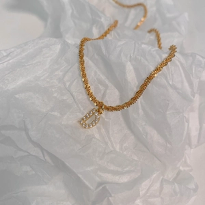 Détail du pendentif lettre D dorée avec zircone cubique brillante et chaîne tressée dorée