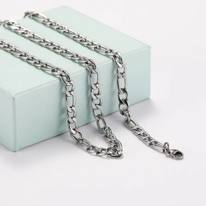 Men's silver stainless steel Figaro cross chain necklace draped over a light blue gift box