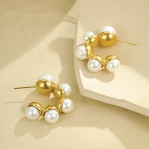 Close-up of C-shaped matte gold stainless steel earrings featuring six round white pearls