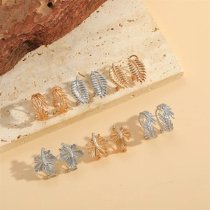 Golden and silver leaf-shaped earrings with zircon accents on a beige stone plate