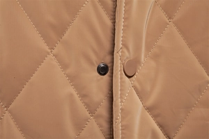 Macro shot of brown quilted jacket featuring diamond patterns and matte snap button