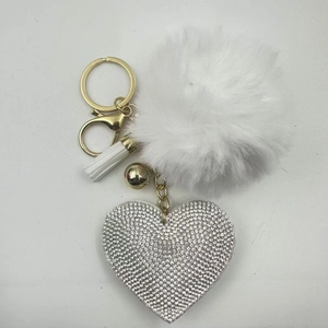 Detail of white faux fur pompom keychain with silver rhinestone heart and gold tassel