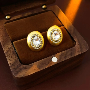 Macro detail of gold oval stud earrings with crystals in a velvet lined wooden box