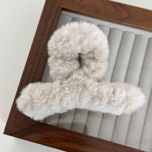 Close-up of soft beige plush claw clip with a fuzzy texture on a wooden jewelry tray