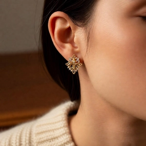 Close-up of 18k gold plated fleur-de-lis earrings with zircons worn by a model