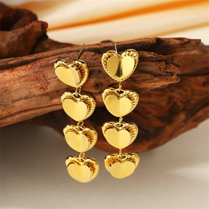 Detailed macro shot of double-layered gold heart tassel earrings on a natural wood base