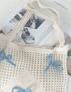 Detail of a creamy white crochet tote bag featuring a light blue knitted bow decoration