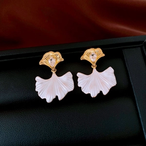 Detailed close-up of ginkgo leaf earring with drop zircon on black leather texture