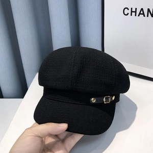 Detail of black wool newsboy hat featuring golden buckles and side leather strap detail